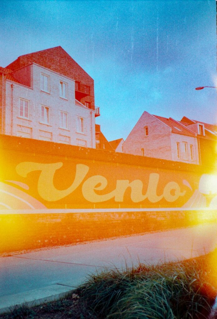 Venlo mural stands in front of colorful buildings.